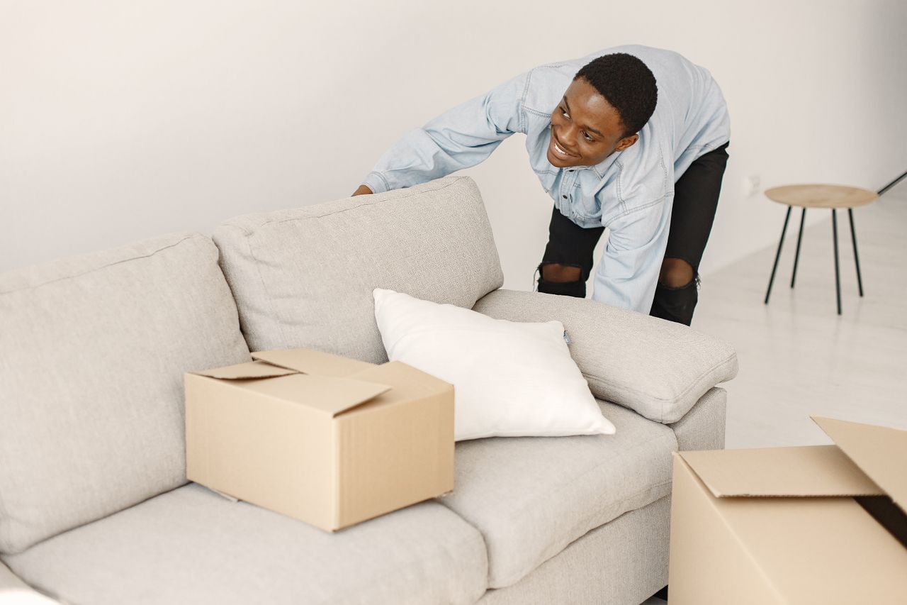 heros-img Young man smiling while arranging cardboard boxes in a modern living room.