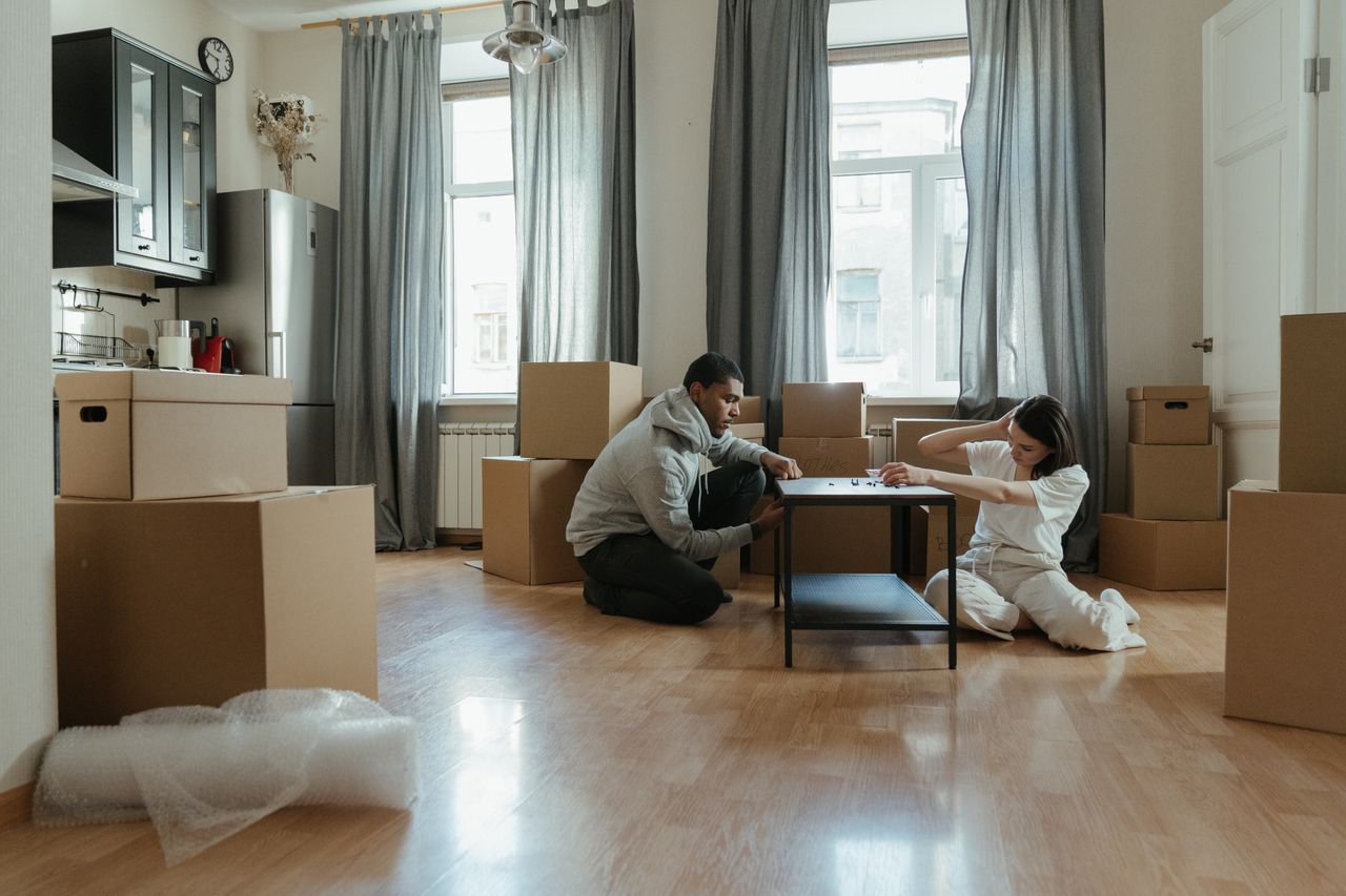 about-us-01 Young couple assembling furniture in their new apartment, surrounded by cardboard boxes.
