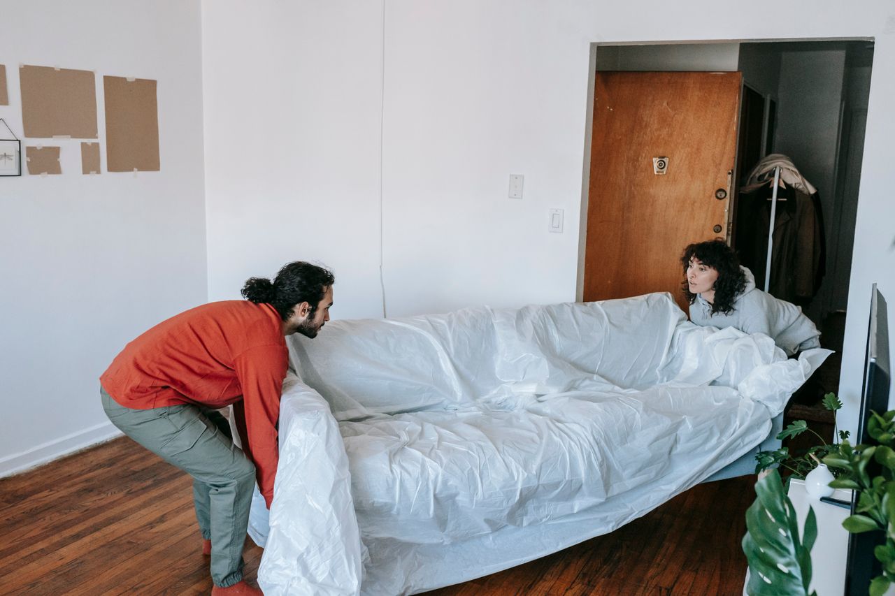 about-us-02 A couple collaboratively lifting a couch while moving into a new apartment.